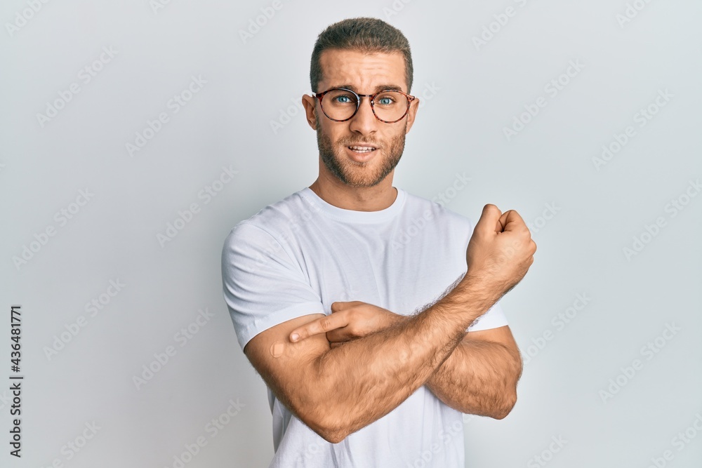 Young caucasian man wearing band aid for vaccine injection clueless and confused expression. doubt concept. Young caucasian man wearing band aid for vaccine injection clueless and confused expression. doubt concept.