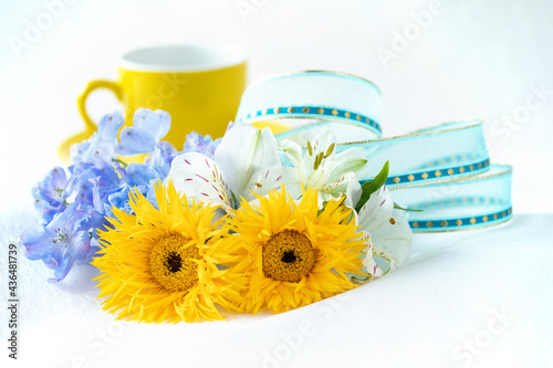 コーヒーとアルストロメリアとデルフィニウムとヒマワリのような細い花びらの黄色のガーベラ（イエロースパイダー）の花束