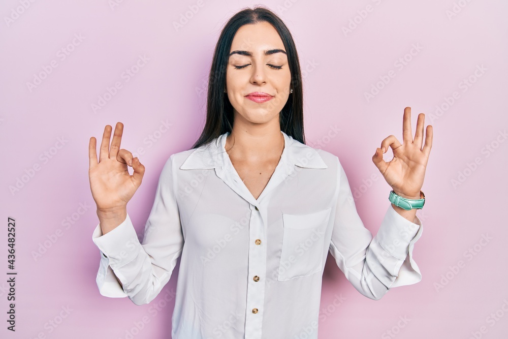Beautiful woman with blue eyes wearing casual white shirt relax and smiling with eyes closed doing meditation gesture with fingers. yoga concept. Beautiful woman with blue eyes wearing casual white shirt relax and smiling with eyes closed doing meditation gesture with fingers. yoga concept.