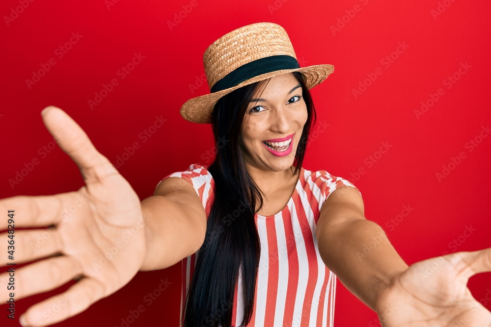 Young latin woman wearing summer hat looking at the camera smiling with open arms for hug. cheerful expression embracing happiness. Young latin woman wearing summer hat looking at the camera smiling with open arms for hug. cheerful expression embracing happiness.
