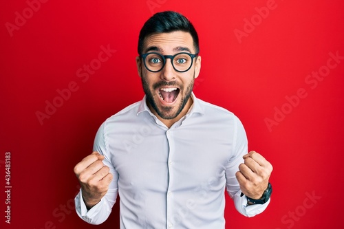 Young hispanic businessman wearing shirt and glasses celebrating surprised and amazed for success with arms raised and open eyes. winner concept. © Krakenimages.com