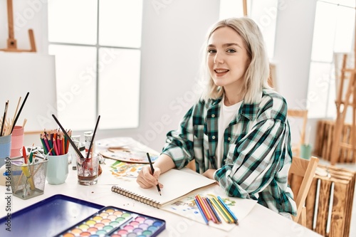 Young artist student girl smiling happy painting sitting on desk at art studio.