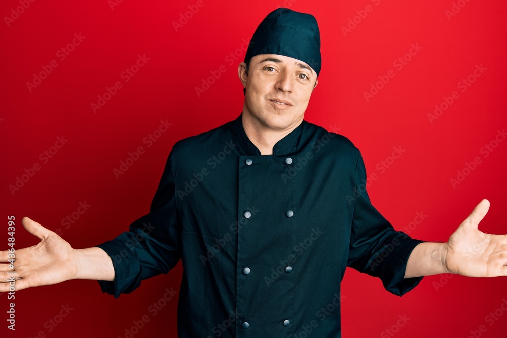 Handsome young man wearing professional cook uniform and hat clueless and confused expression with arms and hands raised. doubt concept. Handsome young man wearing professional cook uniform and hat clueless and confused expression with arms and hands raised. doubt concept.