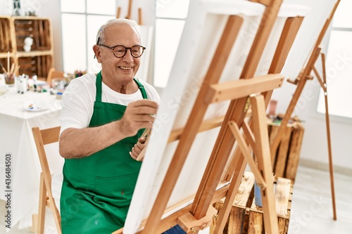 Senior grey-haired artist man smiling happy painting at art studio.