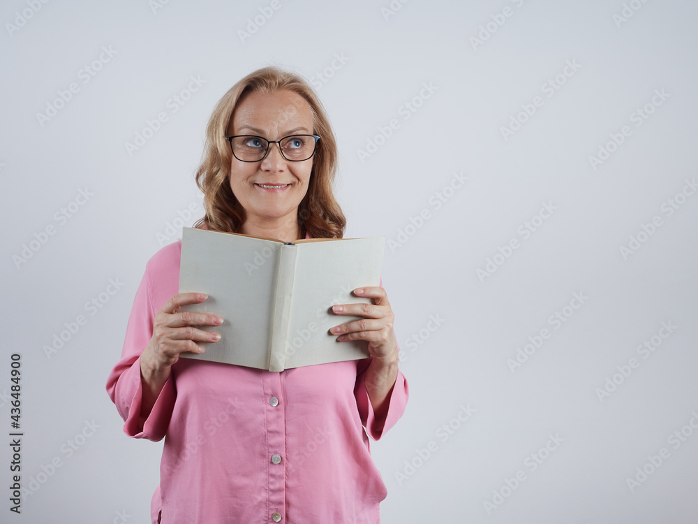 A charming teacher with an open book in his hands, wearing glasses, looking up. Portrait on a gray background. A charming teacher with an open book in his hands, wearing glasses, looking up. Portrait on a gray background.