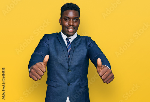 Handsome business black man wearing business suit and tie approving doing positive gesture with hand, thumbs up smiling and happy for success. winner gesture.