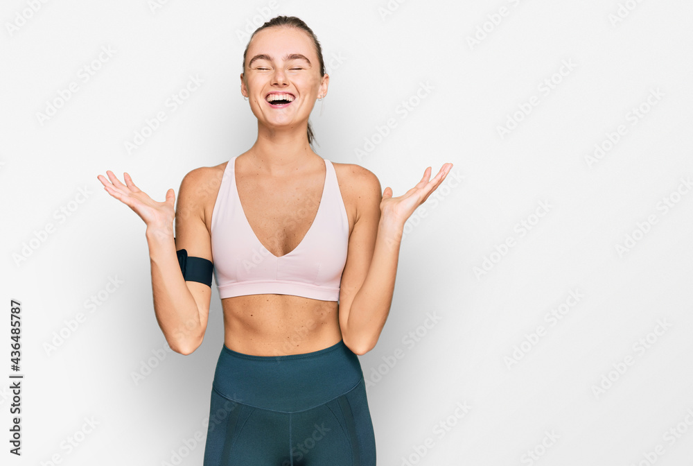 Beautiful young blonde woman wearing sportswear and arm band celebrating mad and crazy for success with arms raised and closed eyes screaming excited. winner concept Beautiful young blonde woman wearing sportswear and arm band celebrating mad and crazy for success with arms raised and closed eyes screaming excited. winner concept