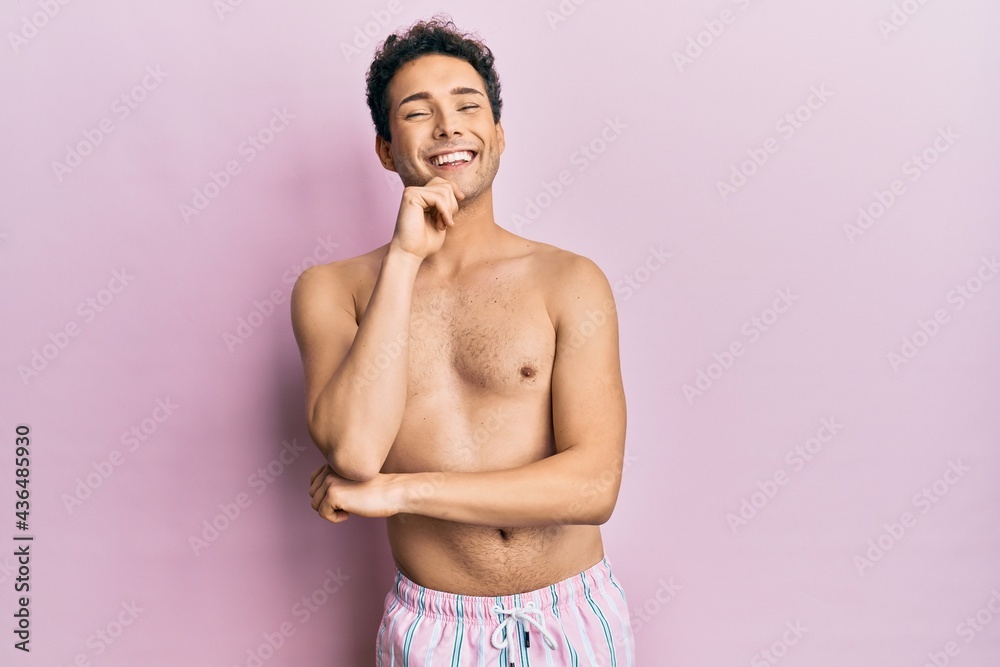 Fototapeta premium Young handsome man wearing swimwear shirtless looking confident at the camera with smile with crossed arms and hand raised on chin. thinking positive.