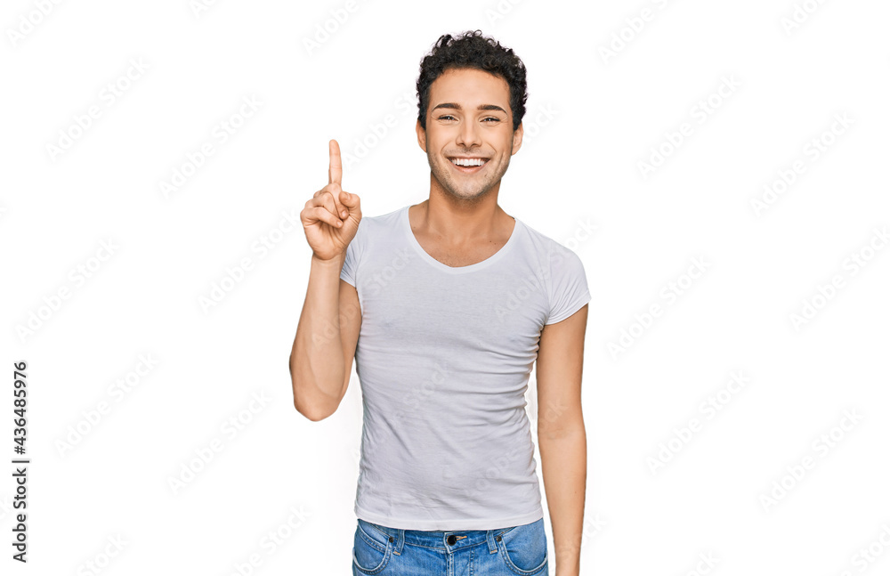 Young handsome man wearing casual white t shirt pointing finger up with successful idea. exited and happy. number one. Young handsome man wearing casual white t shirt pointing finger up with successful idea. exited and happy. number one.
