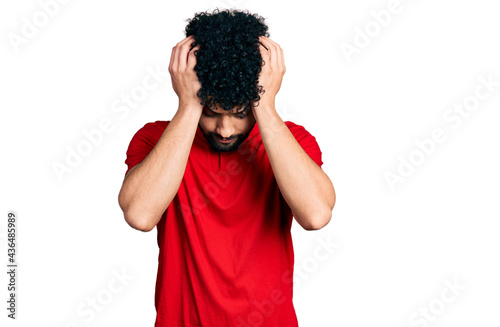 Young arab man with beard wearing casual red t shirt suffering from headache desperate and stressed because pain and migraine. hands on head.