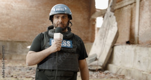 POV Camera view, War journalist correspondent wearing bulletproof vest and helmet reporting live near destroyed building