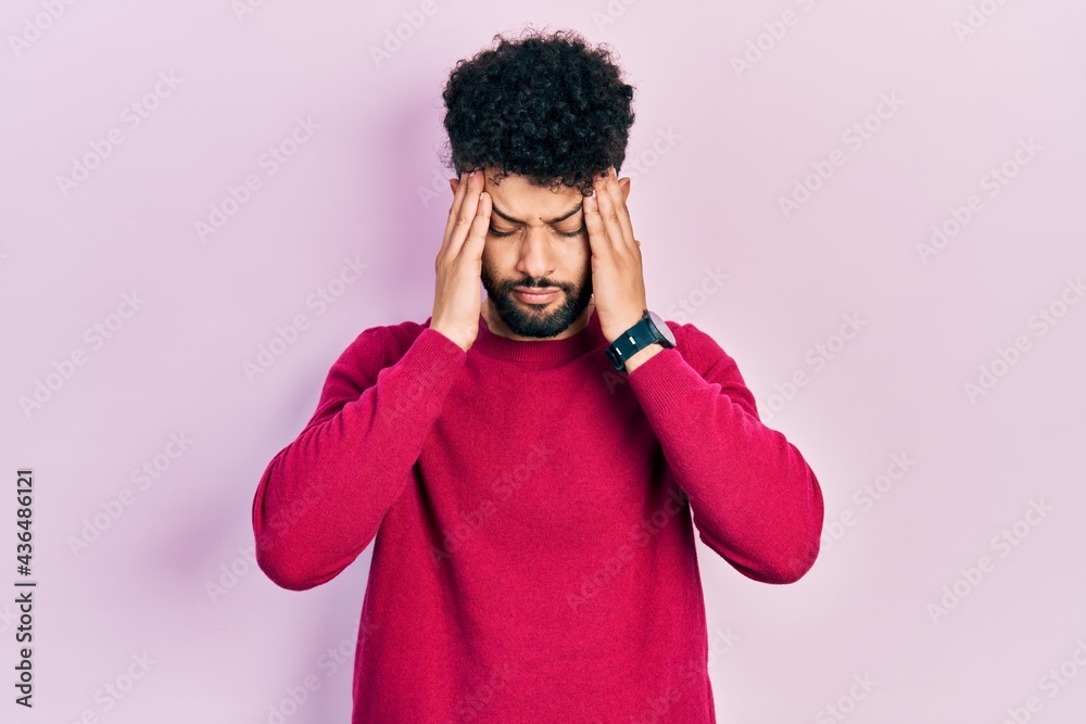 Young arab man with beard wearing casual pink sweater suffering from headache desperate and stressed because pain and migraine. hands on head. Young arab man with beard wearing casual pink sweater suffering from headache desperate and stressed because pain and migraine. hands on head.