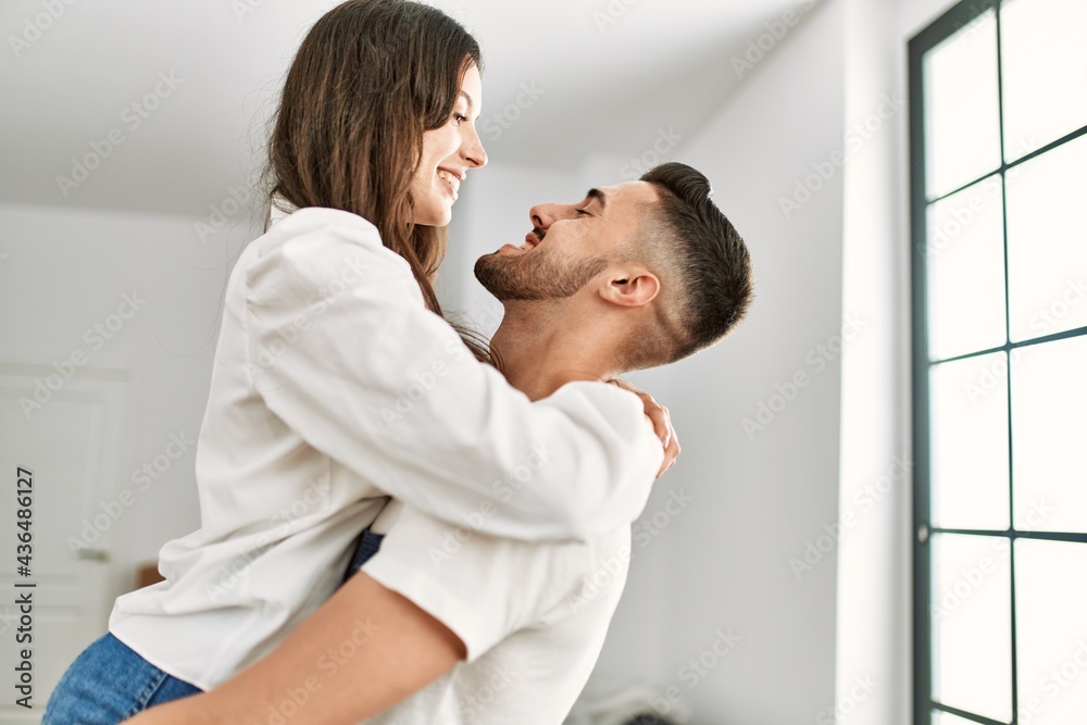 Young hispanic man holding woman in arms and hugging at new home.