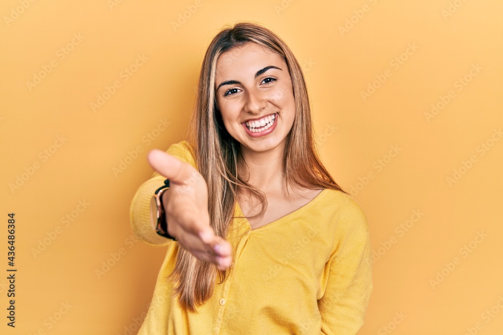 Beautiful hispanic woman wearing casual yellow sweater smiling cheerful offering palm hand giving assistance and acceptance. Beautiful hispanic woman wearing casual yellow sweater smiling cheerful offering palm hand giving assistance and acceptance.