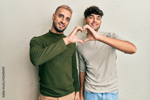 Homosexual gay couple standing together wearing casual clothes smiling in love doing heart symbol shape with hands. romantic concept.