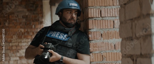 Hispanic male war journalist wearing protective helmet and bulletproof vest gear taking photos during military operation photo