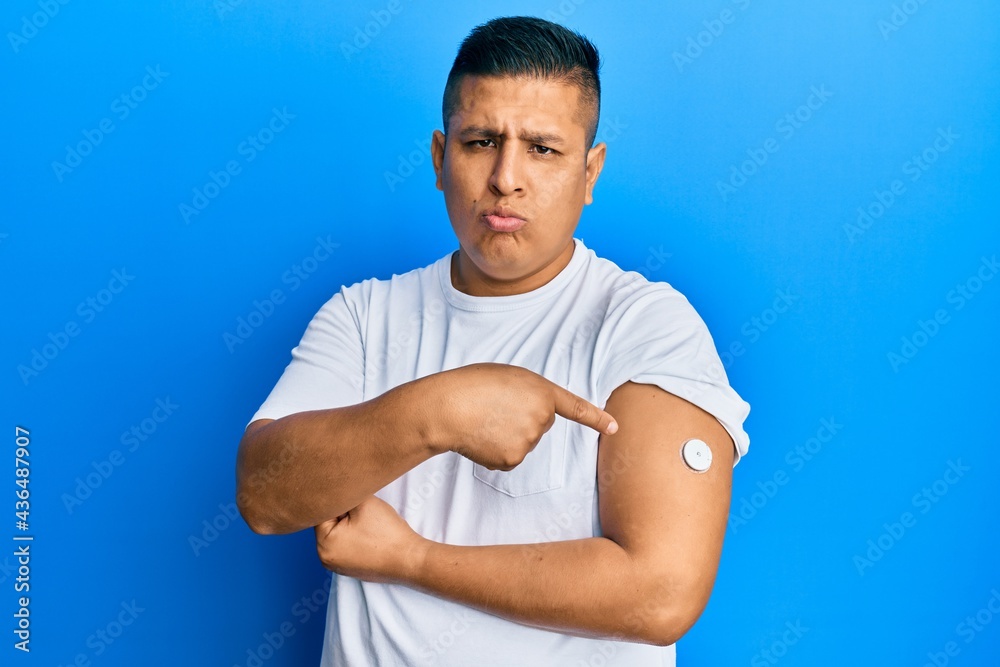 Young latin man using glucose meter button on arm depressed and worry for distress, crying angry and afraid. sad expression. Young latin man using glucose meter button on arm depressed and worry for distress, crying angry and afraid. sad expression.