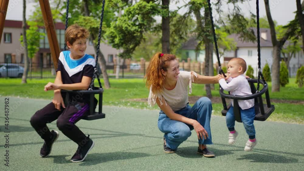 Happy family mom with childs rolls the little child in flight on swing in the park. On weekends, mother and daughter walk. Family walks in park. Kid and young parent. concept of children and family.