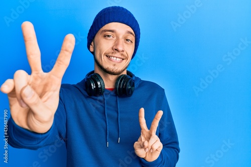 Hispanic young man wearing sweatshirt and headphones smiling looking to the camera showing fingers doing victory sign. number two.