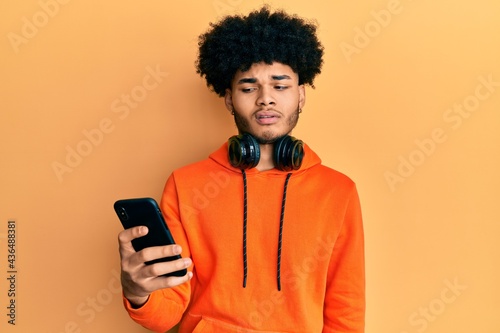 Young african american man with afro hair using smartphone clueless and confused expression. doubt concept.