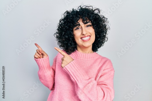 Young middle east woman wearing casual clothes smiling and looking at the camera pointing with two hands and fingers to the side.