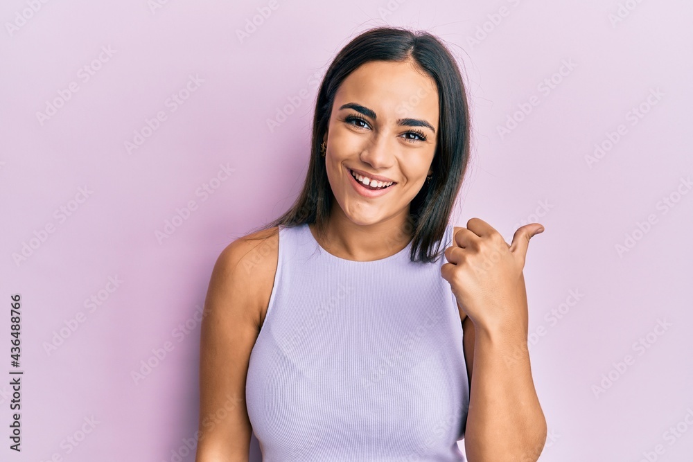 Young brunette woman wearing casual clothes pointing thumb up to the side smiling happy with open mouth Young brunette woman wearing casual clothes pointing thumb up to the side smiling happy with open mouth
