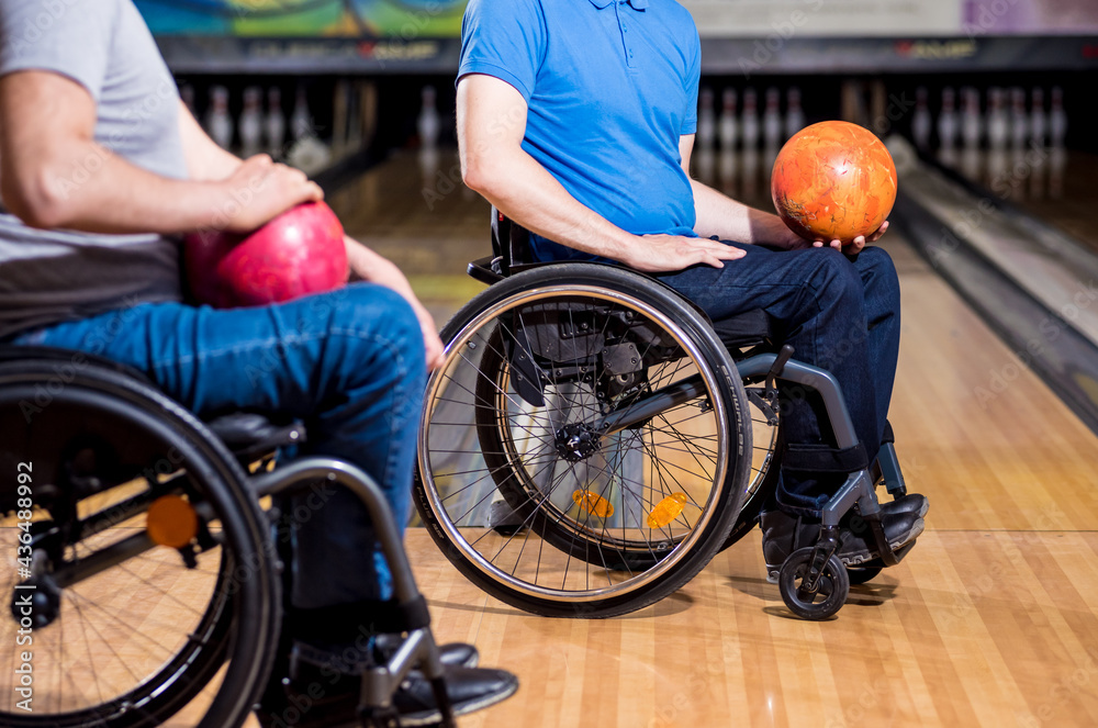 Obraz premium Two young disabled men in wheelchairs playing bowling in the club