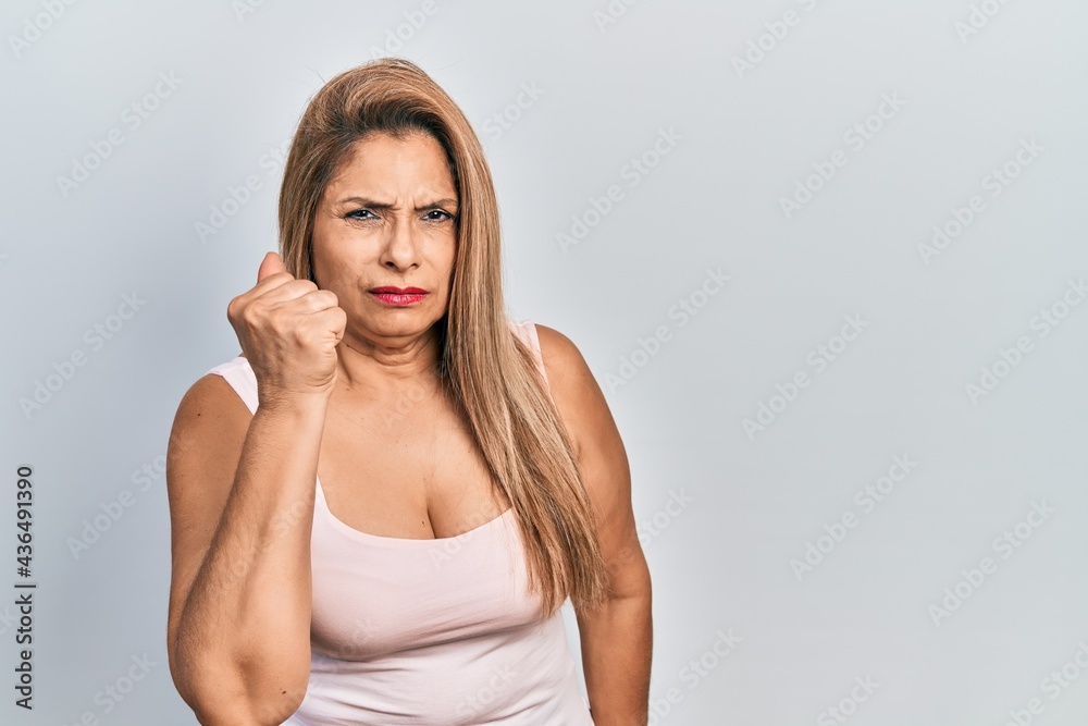 Middle age hispanic woman wearing casual style with sleeveless shirt angry and mad raising fist frustrated and furious while shouting with anger. rage and aggressive concept. Middle age hispanic woman wearing casual style with sleeveless shirt angry and mad raising fist frustrated and furious while shouting with anger. rage and aggressive concept.