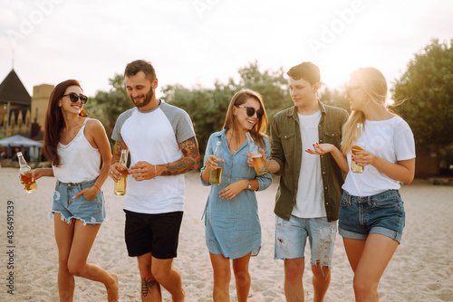 Group of friends cheers and drink beers on the beach. Young friends relaxing on the beath having picnic, toasting with beerus. People, lifestyle, travel, nature and vacations concept. photo