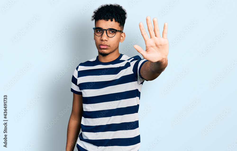 Naklejka premium Young african american man wearing casual clothes and glasses doing stop sing with palm of the hand. warning expression with negative and serious gesture on the face.