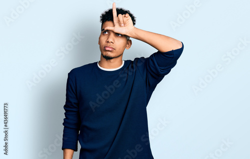 Young african american man wearing casual clothes making fun of people with fingers on forehead doing loser gesture mocking and insulting.