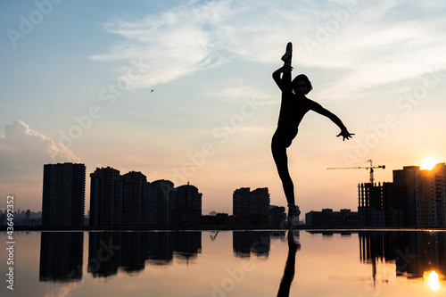 Silhouette of ballerina performing on cityscape and dramatic sunset background. Concept of willpower, control and dream