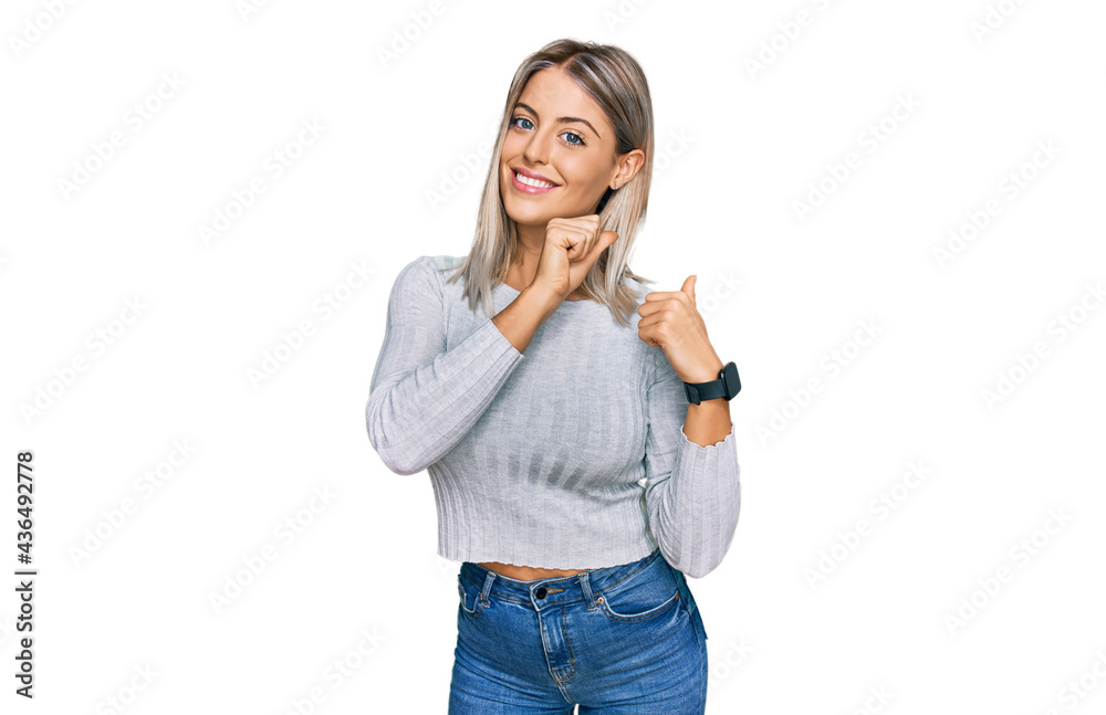 Beautiful blonde woman wearing casual clothes pointing to the back behind with hand and thumbs up, smiling confident Beautiful blonde woman wearing casual clothes pointing to the back behind with hand and thumbs up, smiling confident