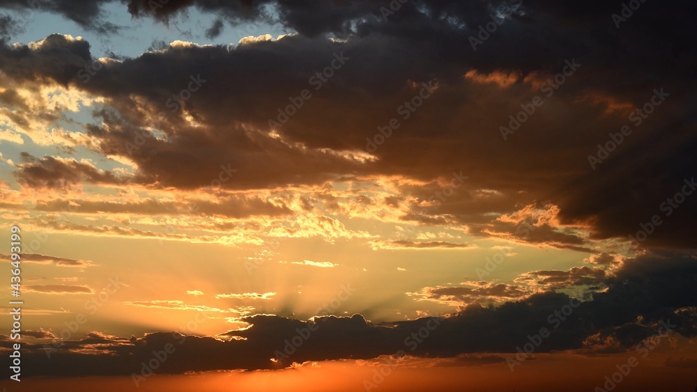 Bright golden sunbeams shining through dark clouds. Orange brown cloudscape of sunset. Dramatic sky while sundown in dusk