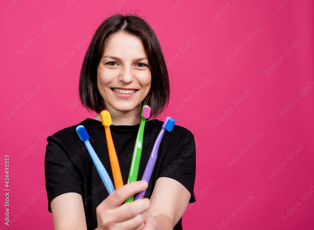 Beautiful happy young woman with different colored toothbrushes on blank pink background Beautiful happy young woman with different colored toothbrushes on blank pink background