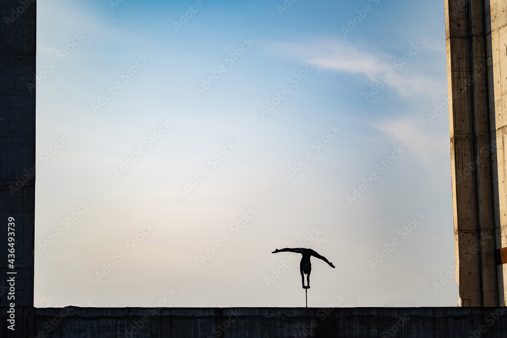 Silhouette of flexible girl dong handstand in split on sky background. Concept of individuality, creativity and outstanding Silhouette of flexible girl dong handstand in split on sky background. Concept of individuality, creativity and outstanding