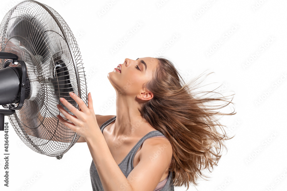 Young woman cooling down with electric fan Photos | Adobe Stock