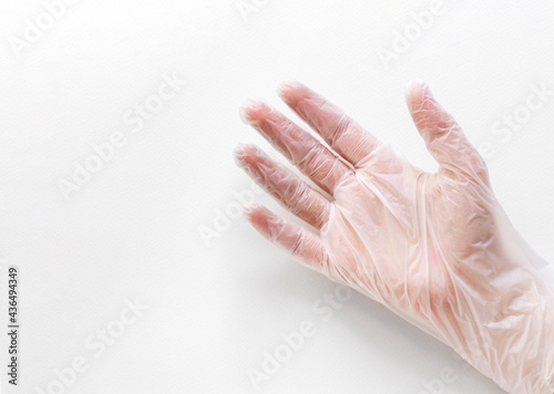 One hand in disposable vinyl glove with open palm above white background with copy space from left side. Safety and selfcare concept.