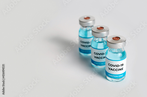 Close up of Covid-19 vaccine vials and syringe on white background. Hand takes one bottle of vaccine. Focus moves quickly to second bottle. Medical vaccination concept