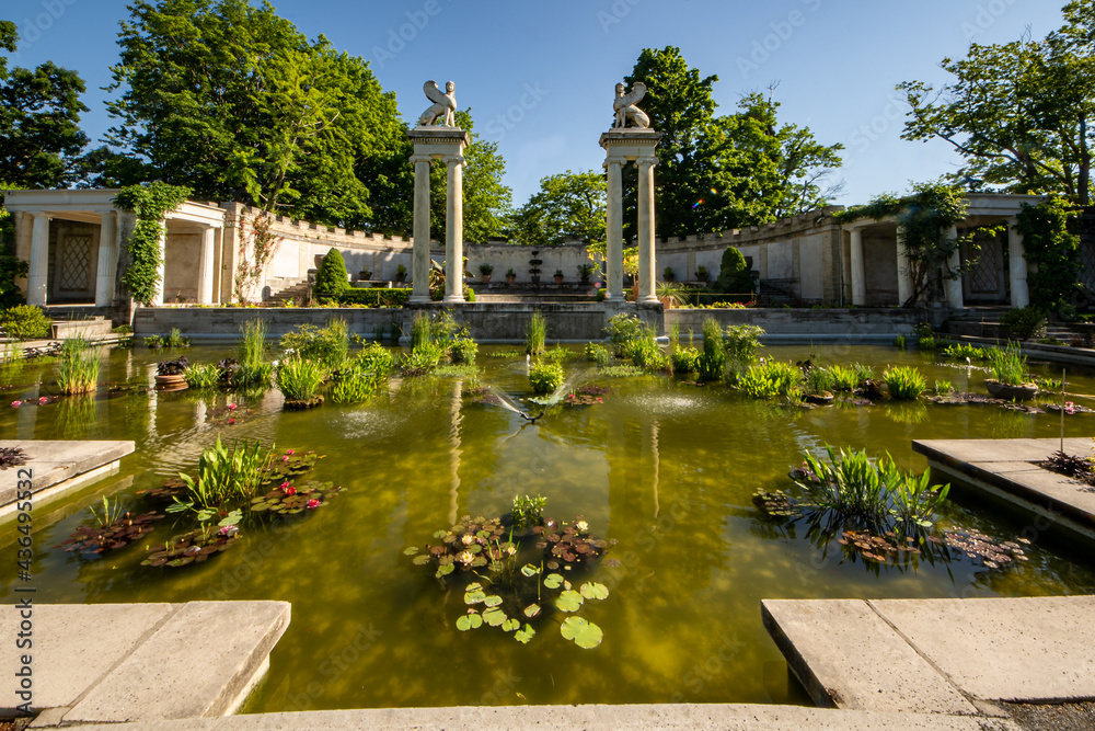Yonkers, NY - USA - May 27, 2021: A view of Untermyer Garden's Amphitheater pool, a large reflecting pool dotted with tropical water lilies and two facing marble sphinxes behind it.