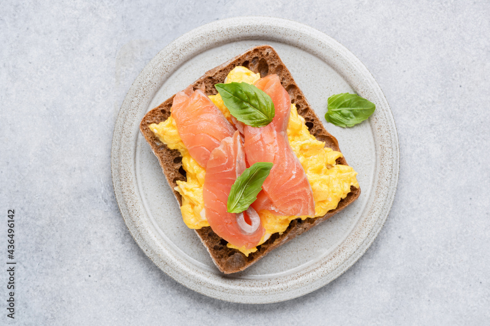Breakfast toast with scrambled eggs and smoked salmon Lox on grey plate, top view. Isolated on grey concrete background. Tasty healthy sandwich with egg and salmon