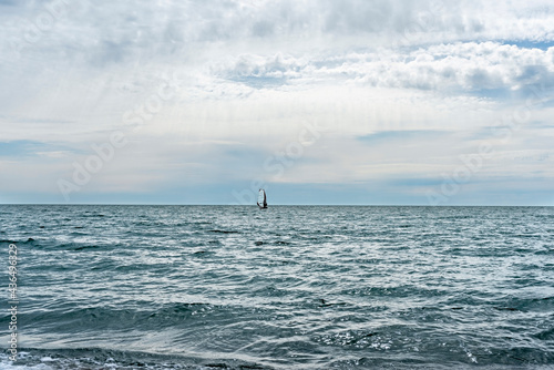Athlete riding windsurf in the distance on blue sea against blue cloudy sky in summer, water sports, active healthy lifestyle, windsurfing, copy space