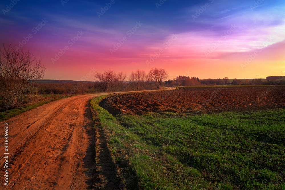Sunset landscape with a dirt road and a meadow