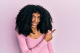 African american woman with afro hair wearing casual pink shirt cheerful with a smile of face pointing with hand and finger up to the side with happy and natural expression on face