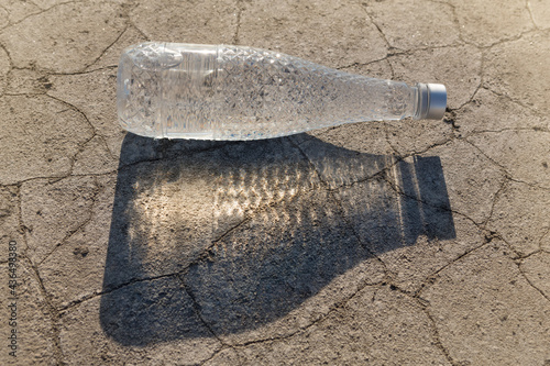 Photography drinking water bottle casts long shadow lying on dry cracked ground