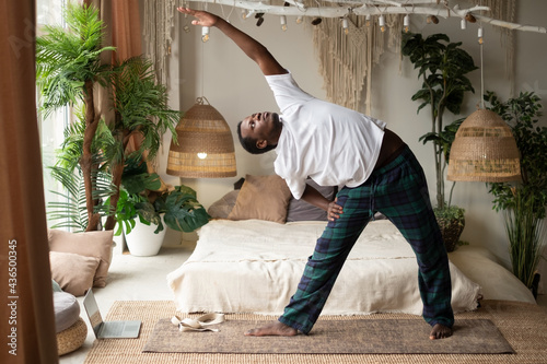 African man practicing yoga doing trikonasana or triangle pose at home photo