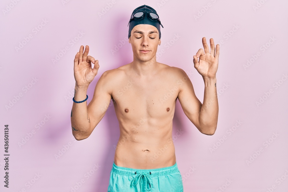 Young hispanic man wearing swimwear and swimmer glasses relax and smiling with eyes closed doing meditation gesture with fingers. yoga concept.