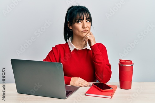 Fotografie Young brunette woman with bangs working at the office with laptop thinking conce
