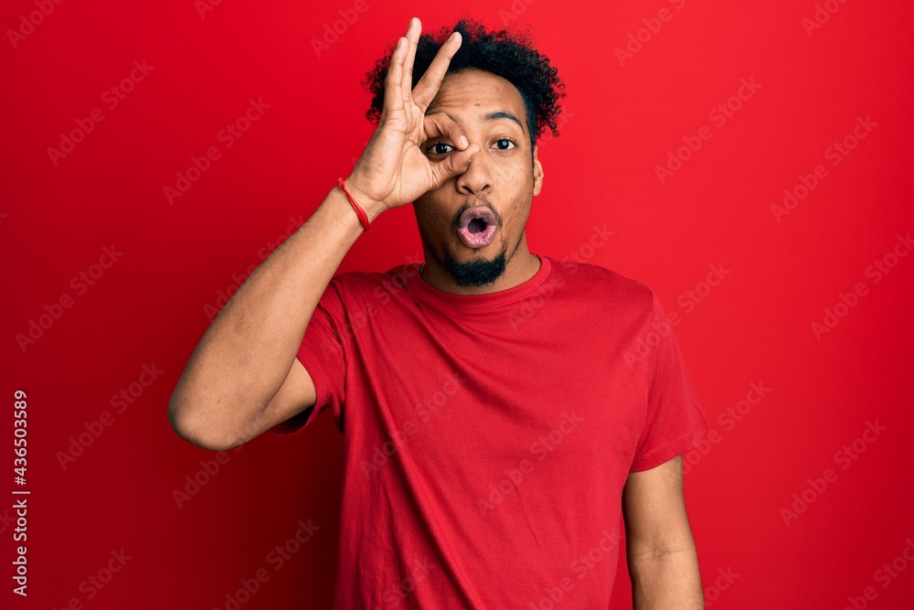 Young african american man with beard wearing casual red t shirt doing ok gesture shocked with surprised face, eye looking through fingers. unbelieving expression. Young african american man with beard wearing casual red t shirt doing ok gesture shocked with surprised face, eye looking through fingers. unbelieving expression.