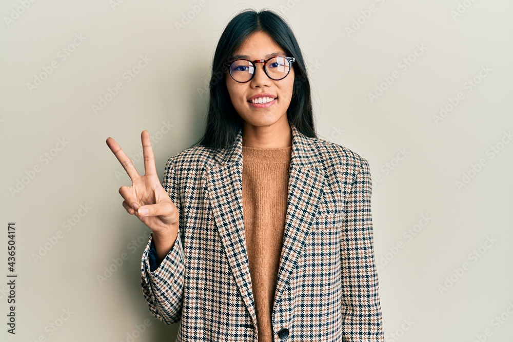 Young chinese woman wearing business style and glasses smiling looking to the camera showing fingers doing victory sign. number two. Young chinese woman wearing business style and glasses smiling looking to the camera showing fingers doing victory sign. number two.